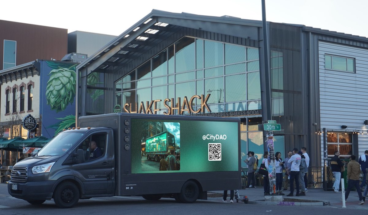 Digital billboard truck in Denver displaying a CityDAO message in front of Shake Shack — the first crowdsourced billboard experiment by The Public Bored