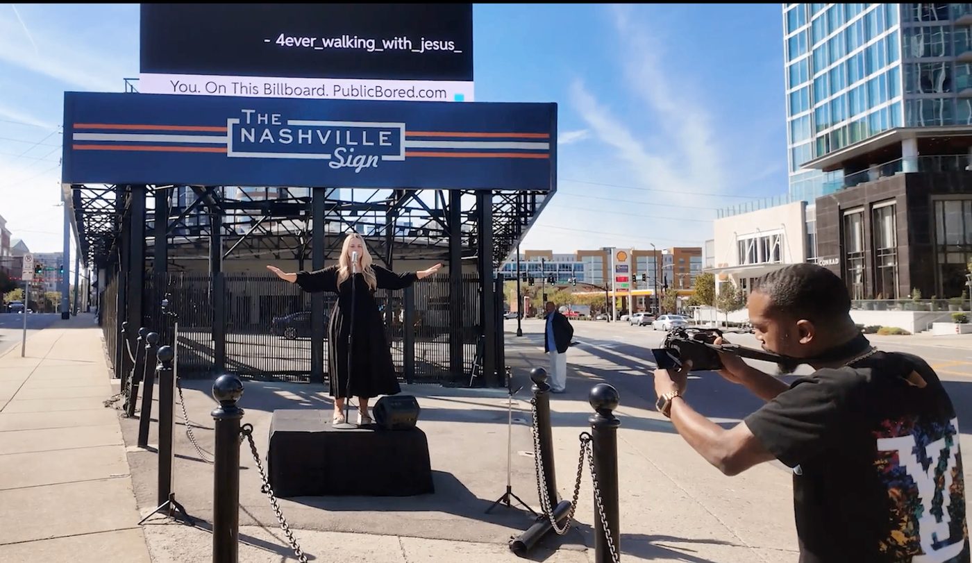 Breanna Nix performing on stage beneath the Nashville billboard while being filmed.