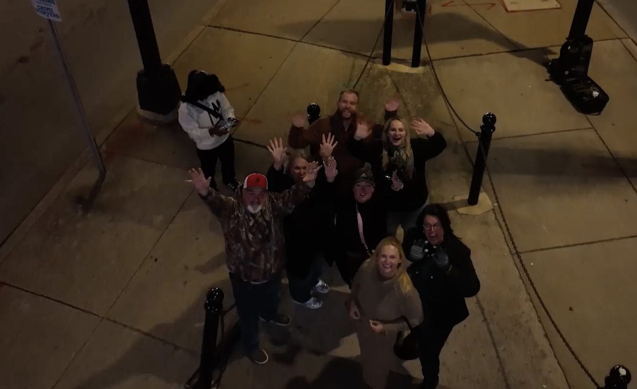 Supporters waving up at the camera from the sidewalk at night.