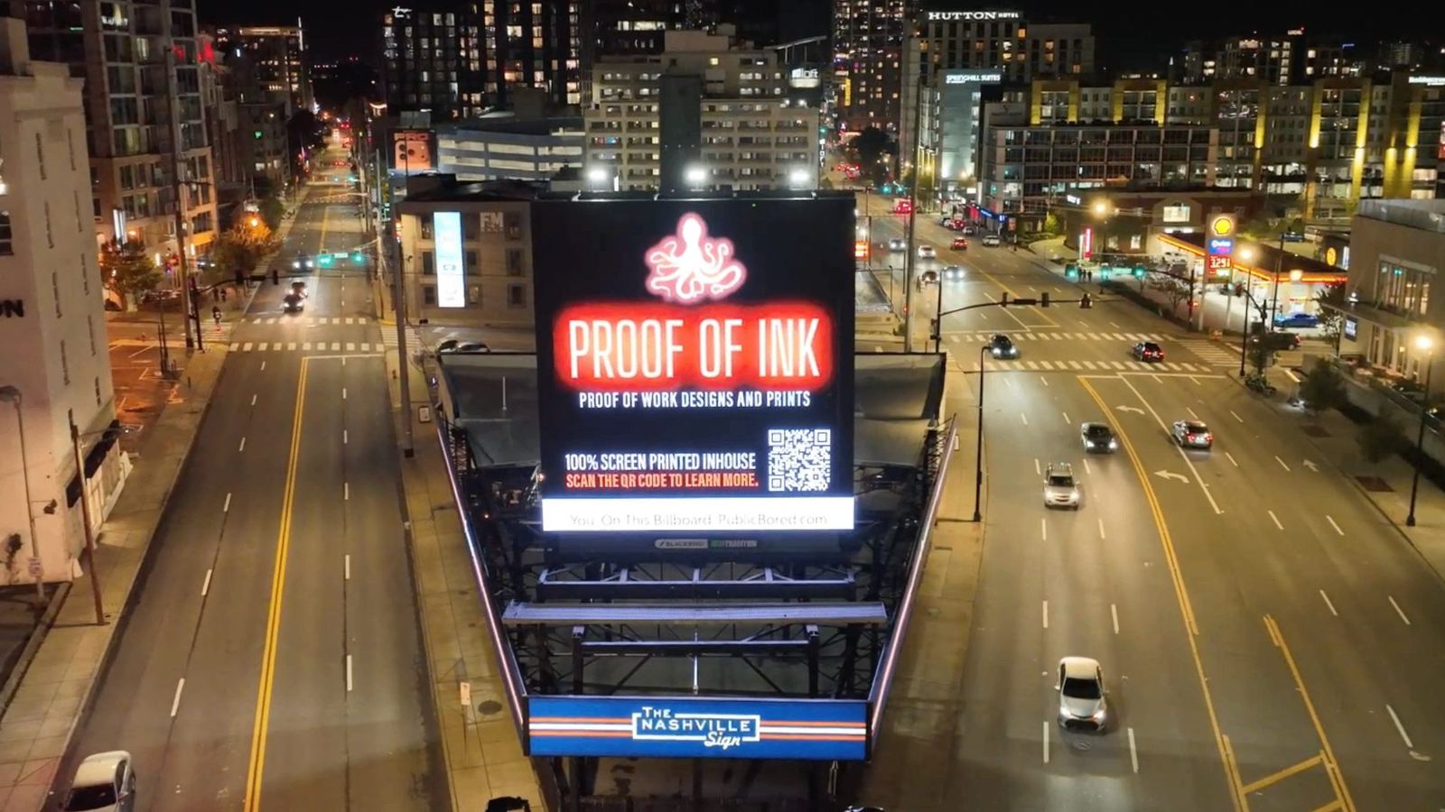 Aerial night view of the Nashville Sign digital billboard displaying a Proof of Ink campaign, surrounded by downtown Nashville skyline and traffic